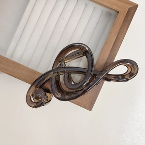 Matte brown acrylic hair claw clip in treble clef design on a wooden stand