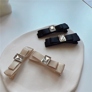 Detail of satin bow hair clips with square crystal centers in black and beige colors