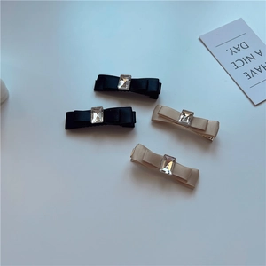 Detail showing elegant satin bow hair clips with rectangular crystal in black and champagne