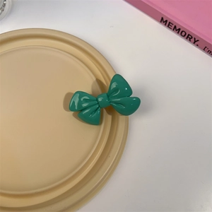 Détail d'une barrette nœud en résine verte avec finition brillante sur plateau déco