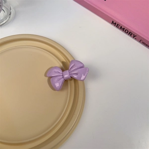 Détail d'une pince à cheveux nœud violet brillant sur un plateau décoratif beige