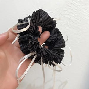 Detailed macro view of black pleated fabric hair scrunchie with white ribbon accents
