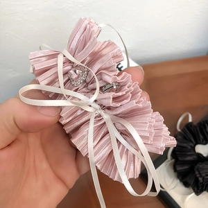 Close-up of pink pleated fabric scrunchie with heart rhinestone and white ribbon detail