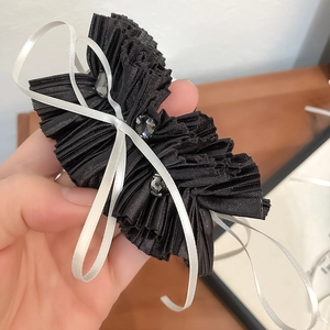 Detail of ruffled black hair tie with sparkling crystals and a white ribbon bow