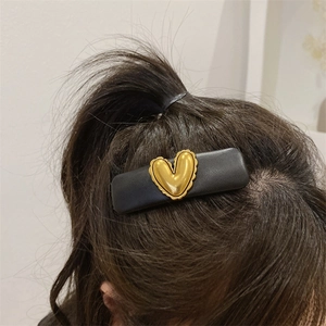 Close-up of a vintage black leather hair clip featuring a 3D golden heart on long dark hair