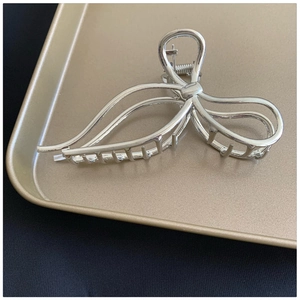 Close-up of a silver bow-knot metal hair claw on a gold tray with polished finish