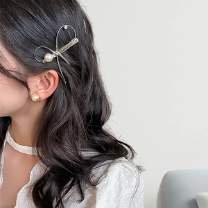 Elegant gold metal bow hair clip with pearl embellishment on a female model side view