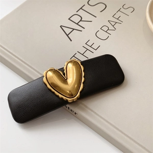 Detail of a black leather hair clip with a golden heart element on a neutral book base