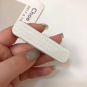 Détail d'une pince à cheveux rectangulaire en tricot blanc montrant la texture du tissu