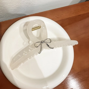 Pince à cheveux beige translucide élégante avec nœud argenté sur assiette en céramique