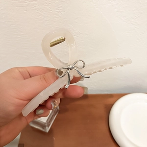 Détail d'une grande pince à cheveux crème translucide avec un nœud en métal argenté