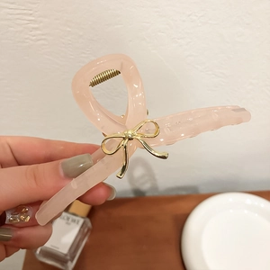 Détail d'une grande pince à cheveux rose translucide ornée d'un nœud en métal doré