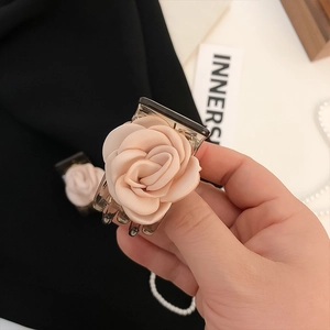 Elegant satin flower hair claw in nude pink finish held by hand for a minimalist aesthetic