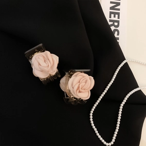 Close-up of elegant satin rose hair claws in nude pink on black fabric background