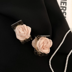Detailed view of two nude pink satin rose hair claws on a textured black backdrop