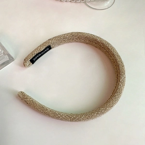 Detail showing braided texture of beige headband with handmade label on inner side