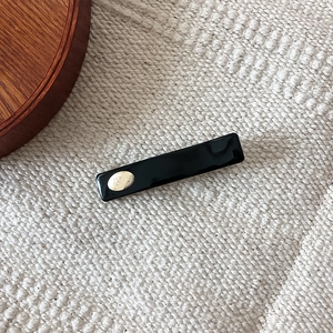 Minimalist black rectangle hair clip with gold logo label on knit fabric background