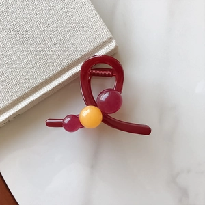 Détail d'une pince à cheveux rouge foncé avec des perles colorées sur fond de marbre