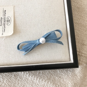 Detail van een blauwe denim haarklem met strik en een witte parel in het midden