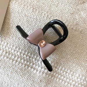 Détail d'une pince à cheveux noire ornée d'un nœud en résine rose et d'un strass brillant