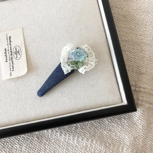 Detail van denim haarklem met wit kantborduurwerk en een klein blauw gehaakt bloemetje