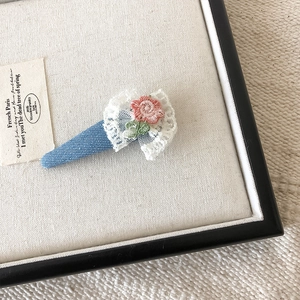 Detail van een bloemen haarklem met kant en een roze geborduurde roos op denim