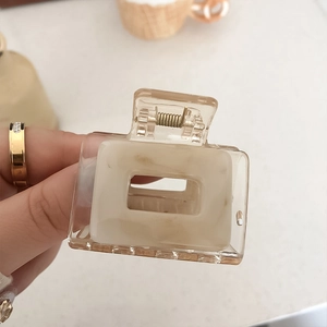 Detail of a square claw clip featuring cream marble texture inside a clear acrylic frame