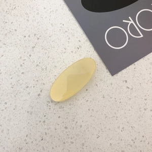 Detail view of a cream-colored oval hair clip on a white marble background texture
