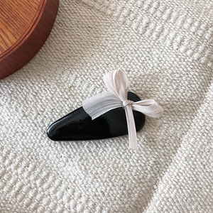 Black glossy teardrop hair clip with soft pink mesh bow on a beige knitted background