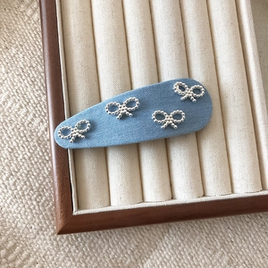 Blue denim fabric hair clip with silver hollow bow charms on a vintage jewelry tray
