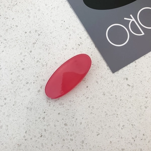 Close-up of a glossy red oval hair clip on a minimalist white stone background