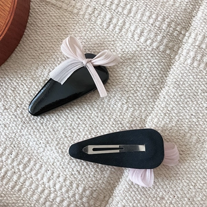 Pink tulle bow hair clips with black glossy base on textured fabric background