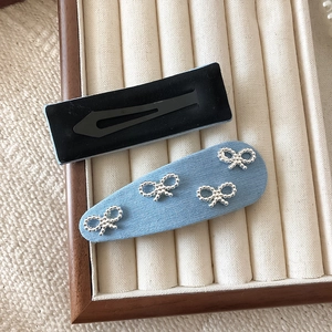 Blue denim fabric hair clip with four silver pearl bow accents on a white tray