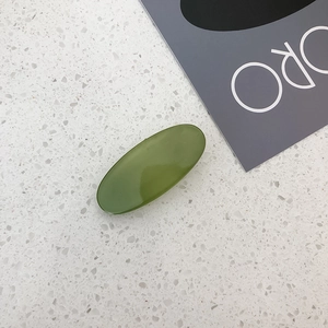 Close-up of a glossy oval candy-colored green hair clip on a minimalist textured background