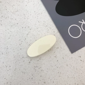 Detailed view of a creamy yellow oval hair clip on a minimalist stone textured background