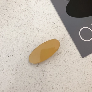 Detail view of mustard yellow oval hair clip on a white marble stone surface