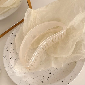 Macro detail of large half-moon hair claw clip in matte cream finish on ceramic plate