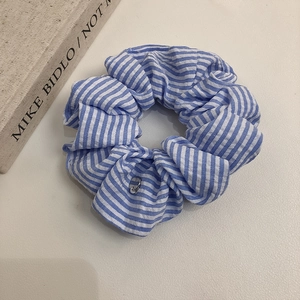 Détail du chouchou en seersucker à rayures bleues avec un petit pendentif en métal