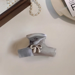 Detail view of a marble texture hair claw clip with a silver metallic bow decoration