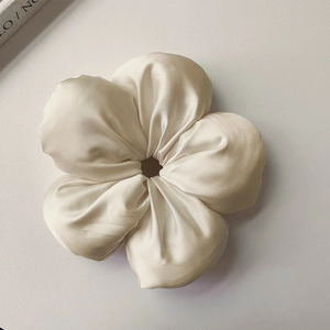 Vista dettagliata di un elastico per capelli a fiore in raso crema con texture lucida e design
