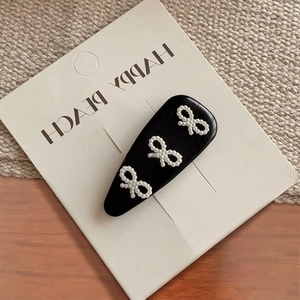 Detalle de una pinza para el pelo BB negra con tres elegantes lazos de perlas blancas