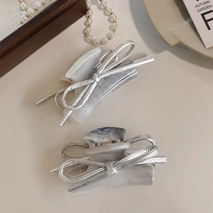 Detail view of silver bow hair claw clips with marble resin texture and gold spring accents