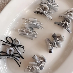 Detail showing ten mini acetate bow hair clips with marble texture in a ceramic tray