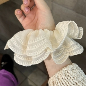 Détail d'un chouchou en dentelle crème avec volants triples et broderie ondulée