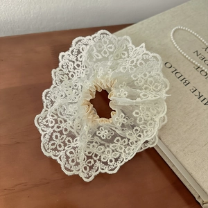 Gros plan détaillé du chouchou en dentelle crème avec broderie florale sur bois
