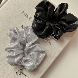Dettaglio di elastici scrunchie metallizzati neri e argento con ciondoli a fiocco
