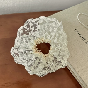 Gros plan du chouchou en dentelle crème avec broderie florale sur bois foncé