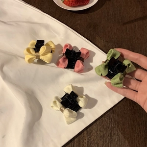 Main tenant quatre mini-pinces à cheveux avec nœuds en tissu jaune, rose, vert et crème