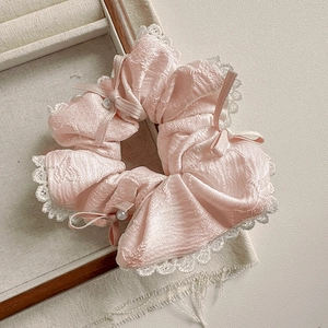 Vue détaillée du chouchou en soie rose avec bordure en dentelle blanche et perle
