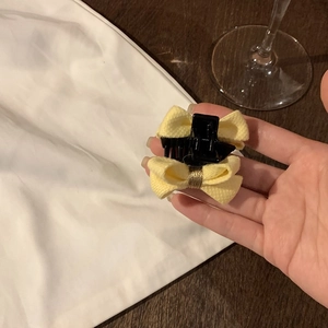 Détail d'une pince à cheveux à nœud en tissu jaune clair tenue à la main par le côté